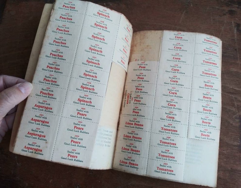 May include: A vintage book of Good Luck Rubber bands for produce. The book has pages of labels for different fruits and vegetables, including peaches, spinach, pears, asparagus, corn, tomatoes, peas, lima beans, and beets. Each label has the year 1929 and the text "Sealed with Good Luck Rubbers".