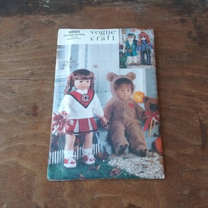Op de afbeelding: Vogue Craft pop-naai-patroon nummer 9895. Het patroon bevat instructies voor het maken van een cheerleader-outfit en een teddybeer-kostuum voor een pop. De patroonhoes toont een pop die een rood-witte cheerleader-outfit draagt en een pop die een bruin teddybeer-kostuum draagt.