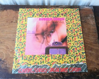 May include: A vinyl record album cover with a yellow, green and red floral pattern border. The album cover features a photo of a person riding a horse with the text "Rubber Rodeo The Hardest Thing" in pink and white letters. The album is by "Cowboy Sabotage Special Dance Edition".
