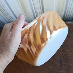 May include: A vintage, iridescent, swirl-patterned, white and gold mixing bowl. The bowl is made of glass and has a smooth, glossy finish.
