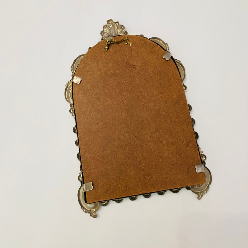 May include: A silver ornate picture frame with a brown backing. The frame has a scalloped edge and a decorative top.