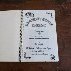 May include: Open cookbook titled "Strawberry Heaven Cookbook" with spiral binding. The cover features handwritten text and illustrations of strawberries. The book was compiled by the Massachusetts Daughters of the American Revolution to benefit Hillside School for Boys.