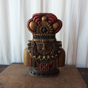 May include: A wooden figurine of a king with a red and gold crown, wearing a black and gold patterned robe. The figurine has a detailed face with a moustache and beard.