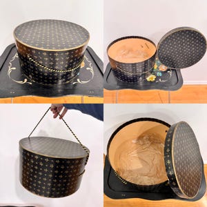 May include: A vintage black hat box with a gold cross pattern and a rope handle. The box has a matching lid and is lined with tan paper. The box is sitting on a black tray with floral accents.