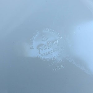 May include: A white Fire King Ovenware Anchor Hocking 7 inch round dish with a blue and white floral design. The bottom of the dish has the Fire King logo and the words "Ovenware" and "Made in USA".