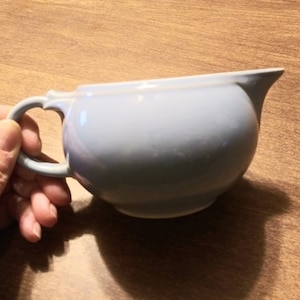 以下が含まれることがあります： 取っ手付きの薄い青色のセラミック製のクリーマー。クリーマーは丸く、表面が滑らかです