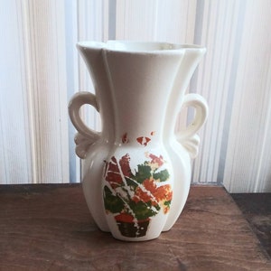 Può includere: Vaso in ceramica bianca con due manici e un disegno floreale in tonalità arancio, verde e marrone.