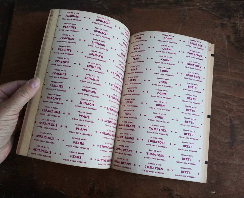 May include: A vintage book of labels for canning jars. The labels are printed in red and white and feature a variety of fruits and vegetables, including peaches, spinach, peas, corn, tomatoes, beets, asparagus, pears, string beans, and lima beans.