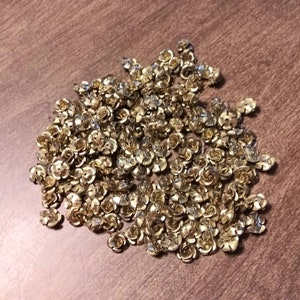 May include: A large pile of gold-colored metal rose-shaped embellishments.