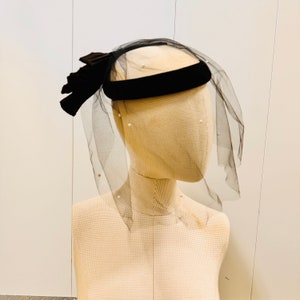 May include: A black velvet headband with a black tulle veil and a black velvet bow. The veil is decorated with small white pearls.