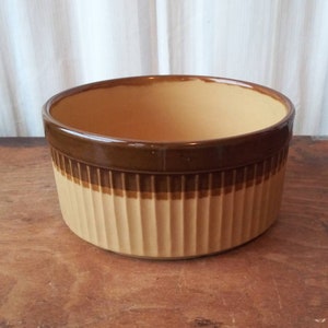 Puede incluir: Un bol de cerámica marrón y beige con un diseño acanalado. El bol tiene un borde marrón y un interior beige.