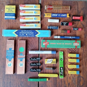 Może przedstawiać: Zbiór vintage'owych ołówków do rysowania i pisania w różnych kolorach i markach, w tym Scripto, Mongol, Eversharp i Sheaffer. Ołówki są zapakowane w pudełka i tuby, niektóre z nazwą marki i rodzajem ołówka.