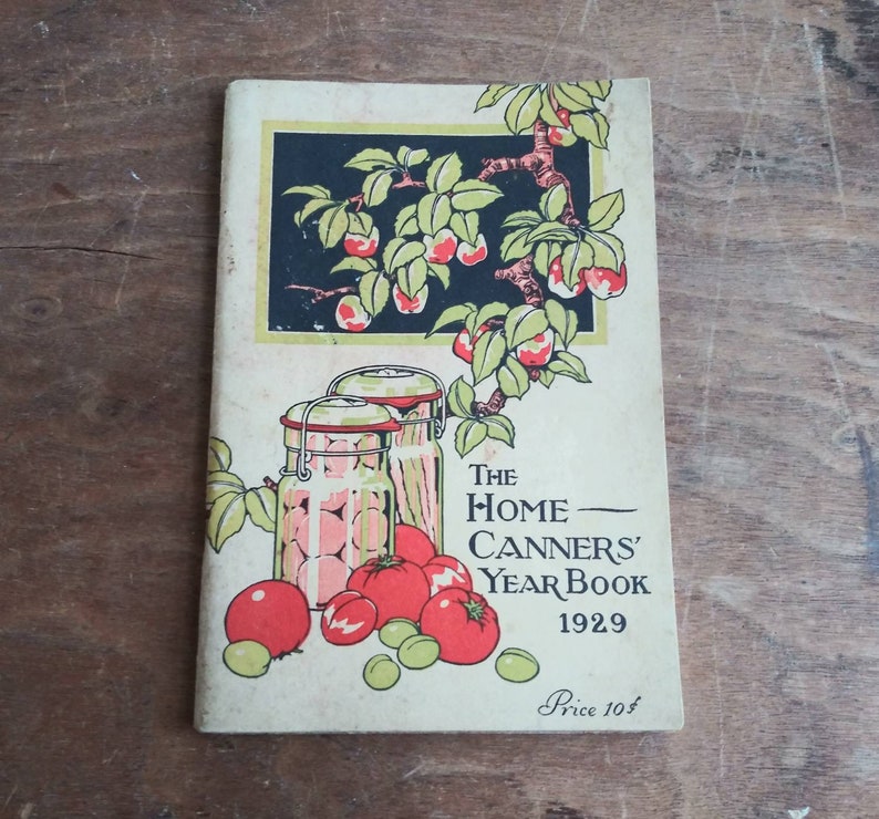 May include: Vintage book cover with a red, green, and black illustration of jars of fruit and a branch of apples. The title is "The Home Canners' Year Book 1929" with the price "Price 10&cent;".