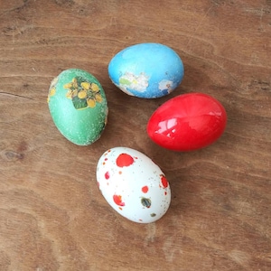 May include: Four Easter eggs decorated with different patterns. One egg is green with yellow flowers, one is blue with white flowers, one is red, and one is white with red and orange splatter paint.