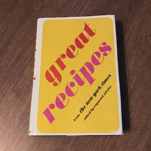 Puede incluir: Un libro amarillo con el título "great recipes" en letras rojas y rosas. El libro es de "the new york times" y editado por Raymond Sokolov.