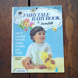 May include: A vintage "Fairytale Baby Book" by Susan Bates, featuring a baby in a white knit sweater. The cover includes text about hand-knit designs for babies up to 3 years, with sizes 18-22 inches (46-56cm). The book has a blue background with illustrations.