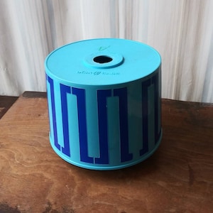 May include: A blue and dark blue plastic container with a round top and a hole in the center. The container has a repeating pattern of vertical stripes.