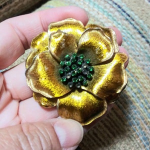 Könnte beinhalten: Eine goldfarbene Blumenbrosche mit einem grünen Strassstein-Zentrum.