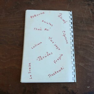 May include: A white notebook with red handwritten words in various languages, including "La Fresa" and "Fragola". The notebook is open, revealing the pages and the spiral binding on the left side. The background is a dark wooden surface.