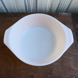 May include: A white, round baking dish with two handles. The dish is made of glass and has a slight pink tint.