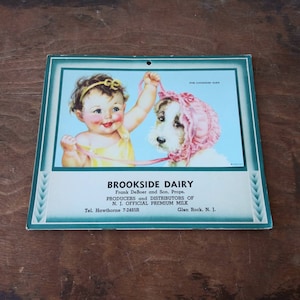 May include: Vintage advertisement for Brookside Dairy, featuring a baby girl in a yellow dress holding a leash attached to a white puppy wearing a pink bonnet. The text reads "For Goodness Sake", "Brookside Dairy", "Frank DeBoer and Son. Props.", "Producers and Distributors of", "N.J. Official Premium Milk", "Tel. Hawthorne 7-2485R", and "Glen Rock, N.J."