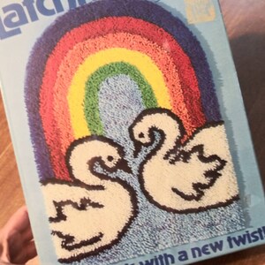 May include: A latch hook kit featuring a rainbow with two white swans in front of it. The kit includes yarn and instructions. The text on the box reads "Latch Hook with a new twist!"