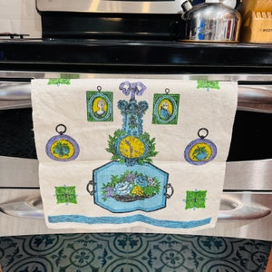 Puede incluir: Un paño de cocina blanco con un diseño azul, verde y amarillo que presenta un reloj, flores y retratos. El diseño recuerda a una esfera de reloj vintage.