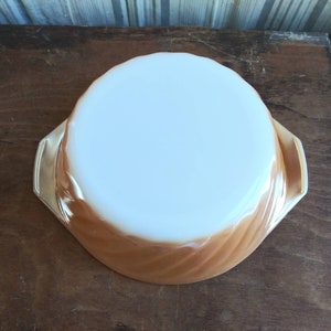 May include: A brown and white swirl pattern glass baking dish with two handles. The dish is empty and sitting on a wooden surface.