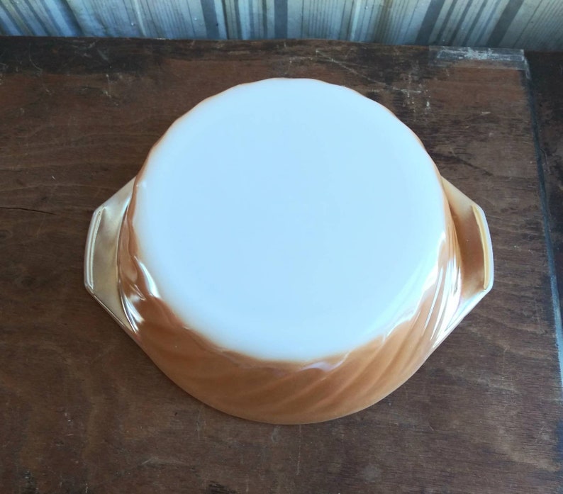 May include: A brown and white swirl pattern glass baking dish with two handles. The dish is empty and sitting on a wooden surface.