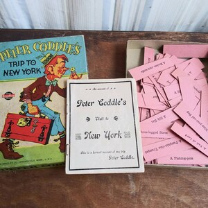 May include: A vintage board game called "Peter Coddle's Trip to New York" with a cartoon illustration of a boy carrying a suitcase. The game includes a booklet and a box of pink cards with text.