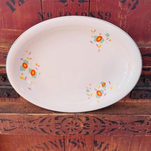 Puede incluir: Una fuente ovalada blanca con borde plateado y un diseño floral en tonos naranja, verde, amarillo y morado.