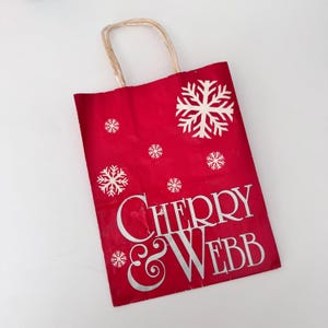 May include: Red paper shopping bag with white snowflakes and the text "CHERRY & WEBB" printed on it.