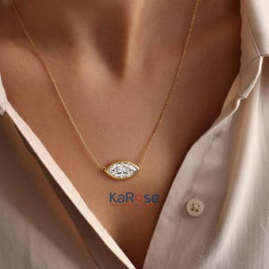 May include: A gold necklace featuring a marquise-cut diamond pendant. The diamond is set in a bezel setting and hangs from a delicate gold chain. The necklace is displayed against a neutral background, highlighting the jewelry's elegance. The brand name "KaRose" is visible.
