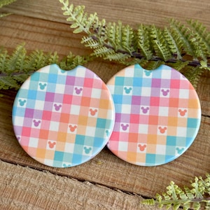 May include: Two round, colorful, gingham patterned coasters with a white background and a repeating pattern of small, white Mickey Mouse heads. The coasters are made of ceramic and have a smooth, glossy finish.
