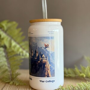 May include: White travel mug with a bamboo lid and a clear glass straw. The mug features a colorful illustration of a castle on a cliff with a dragon flying overhead. The text "War College" is printed on the mug.