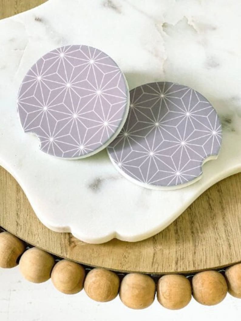 May include: Two gray and white geometric patterned coasters. The coasters have a white outline and a gray background with a white geometric pattern.