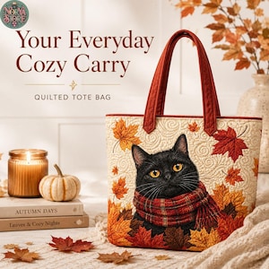 Könnte beinhalten: Eine gesteppte Tragetasche mit einem schwarzen Katzenmotiv, die einen rot karierten Schal trägt, umgeben von orangefarbenen und roten Herbstblättern auf cremefarbenem Grund. Die Tasche hat zwei dunkelrote Stoffgriffe und eine Steppstruktur.