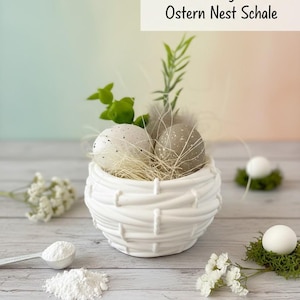 Può includere: Ciotola a nido pasquale in ceramica bianca con uova maculate, vegetazione e piume. La ciotola ha un design intrecciato. L'immagine include il testo "Handmade Raysin Deko Ostern Nest Schale".