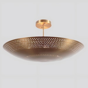 May include: A brass-colored, bowl-shaped ceiling light fixture. The fixture has a perforated design with small, evenly spaced holes. It is suspended from a round ceiling mount by a slender rod. The overall design is modern and minimalist.