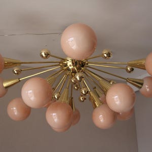 May include: A mid-century modern ceiling light fixture with a brass finish and multiple peach-colored globe shades. The light has a starburst design, with the globes radiating outwards from a central hub.