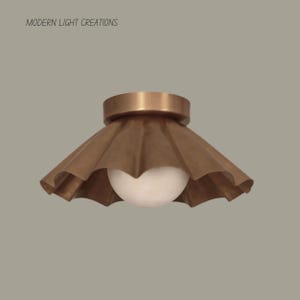 Può includere: Una plafoniera color bronzo con paralume plissettato e globo bianco. L'apparecchio ha una base circolare e il testo "MODERN LIGHT CREATIONS" è visibile.