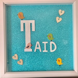 May include: A framed artwork with a turquoise glitter background. The word "AID" is spelled out with individual white letters. Wooden birds and hearts are scattered around the letters. The letter "T" is also in white.