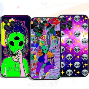 May include: Three phone cases with alien-themed designs. One case features a green alien girl with three eyes, another showcases an alien in a colorful urban setting, and the third displays a pattern of alien faces and stars on a purple background.