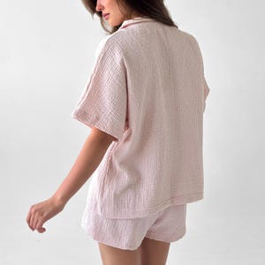 May include: A light pink pajama set, featuring a short-sleeved button-up shirt and matching shorts. The fabric has a textured, crinkled appearance. The set is designed for comfort and relaxation.
