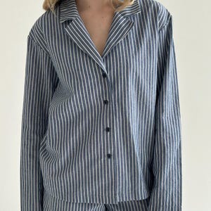 May include: A blue and white striped pajama shirt with a collared neckline and button-down front. The long-sleeved shirt features vertical stripes and is made of a soft, lightweight fabric. The pajama top is part of a matching set.