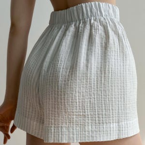 May include: Light blue shorts with an elastic waistband. The shorts are made of a textured, crinkled fabric. The shorts have a relaxed fit and a simple design, suitable for casual wear.