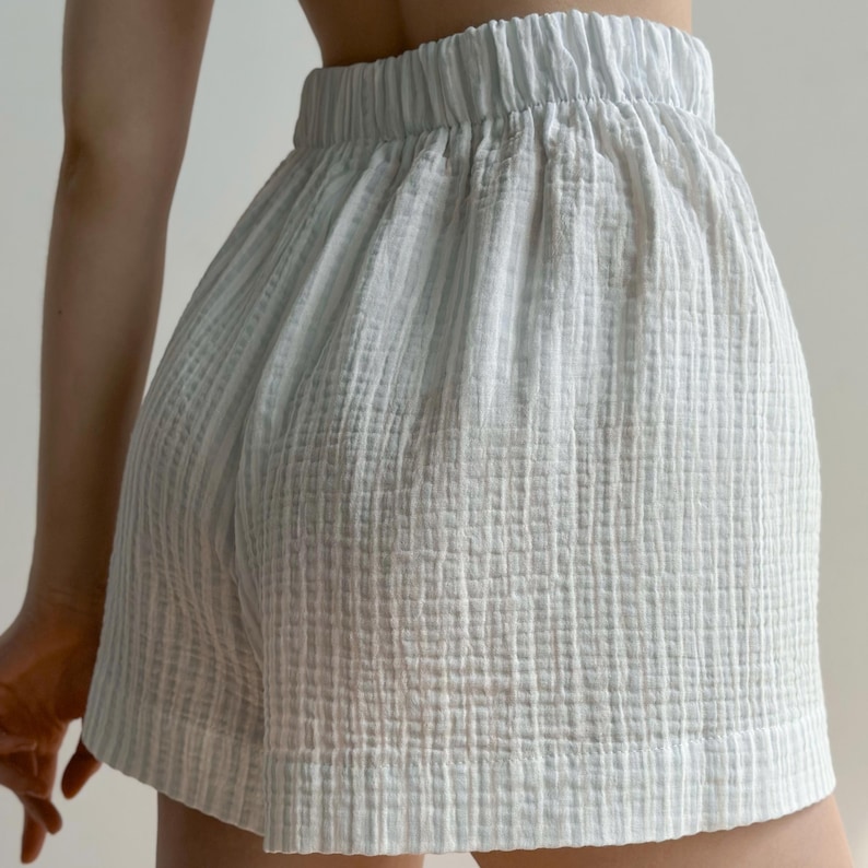 May include: Light blue shorts with an elastic waistband. The shorts are made of a textured, crinkled fabric. The shorts have a relaxed fit and a simple design, suitable for casual wear.