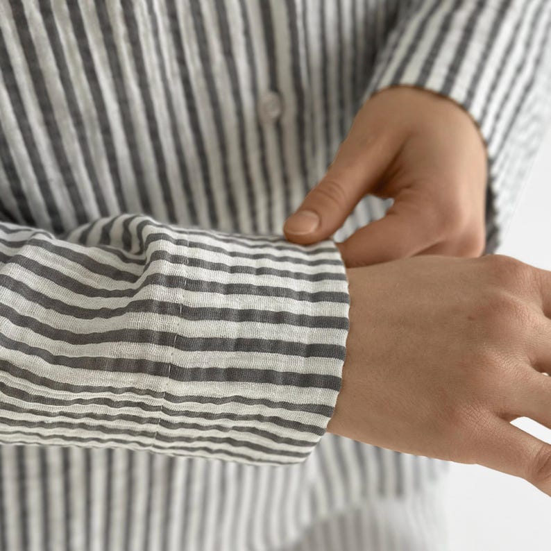 Op de afbeelding: Een grijs en wit gestreept button-down overhemd. Het shirt met lange mouwen heeft een klassieke kraag en is gemaakt van een lichte stof. De afbeelding toont de manchet van het shirt dat wordt aangepast.