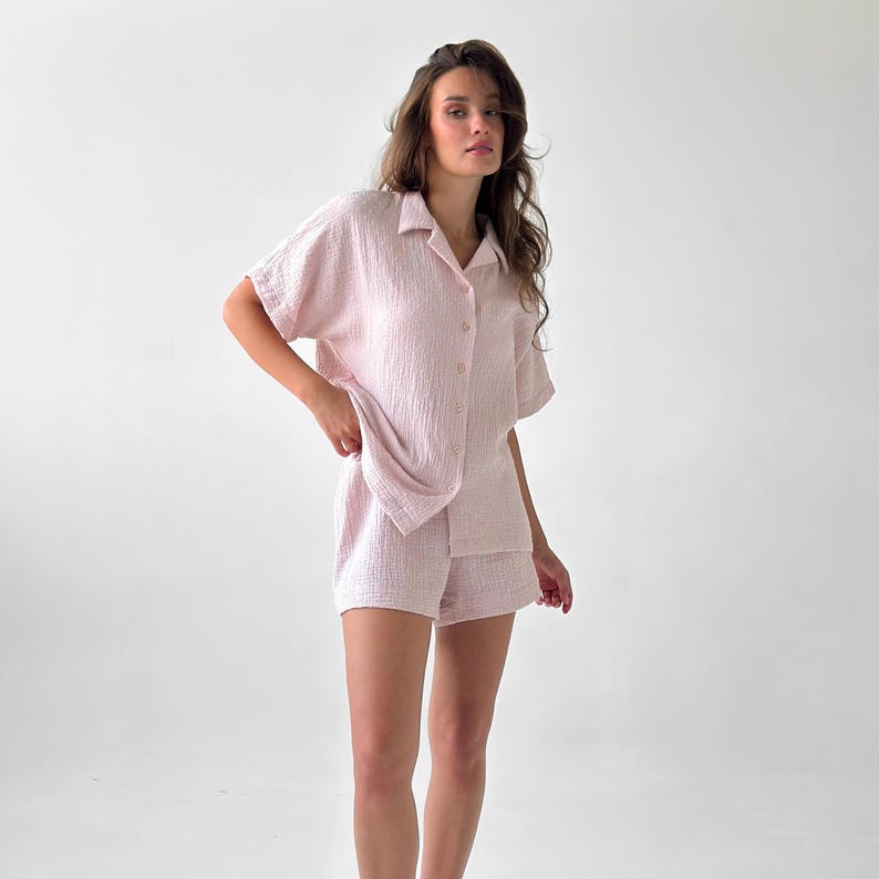 May include: A light pink pajama set, featuring a short-sleeved button-down shirt and matching shorts. The fabric has a textured, crinkled appearance. The set is designed for comfort and relaxation.