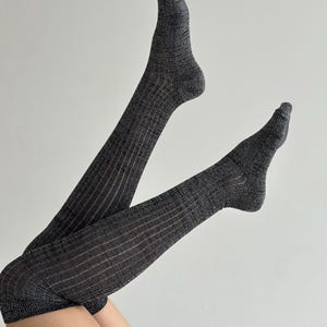 May include: A pair of charcoal gray, ribbed-knit over-the-knee socks. The socks are pulled up, showcasing the texture and design. The ribbed pattern runs vertically along the length of the socks.